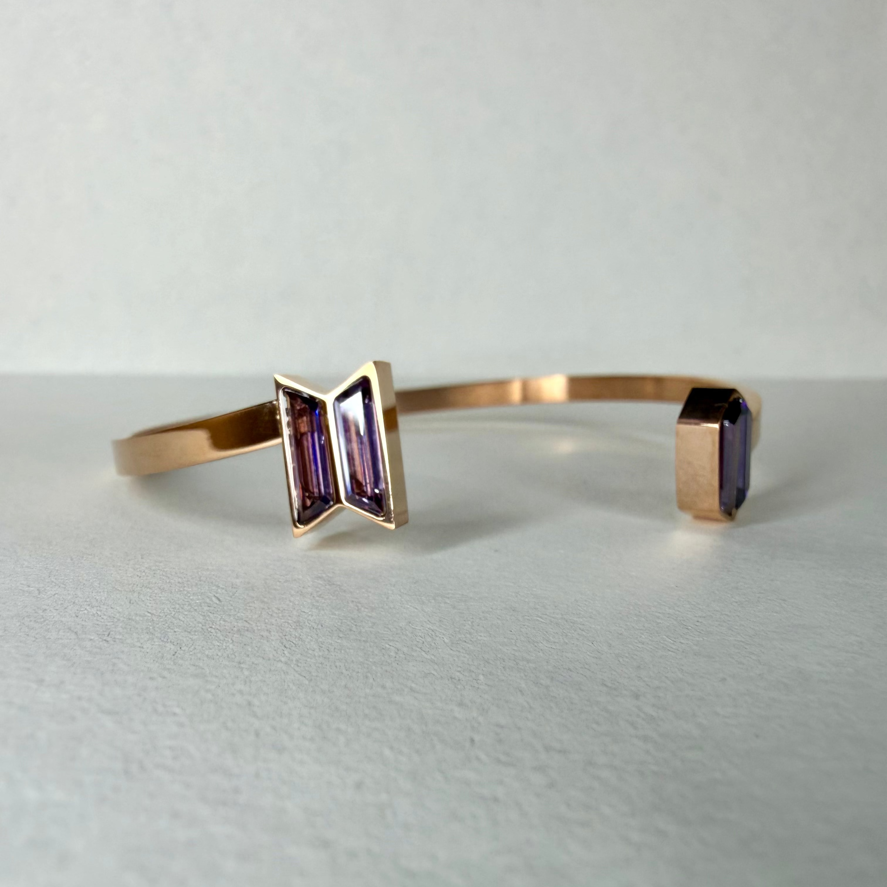 Rose gold bracelet with purple gemstones on a light gray background